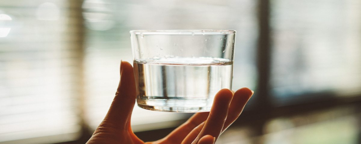 person holding clear glass cup with half-filled water